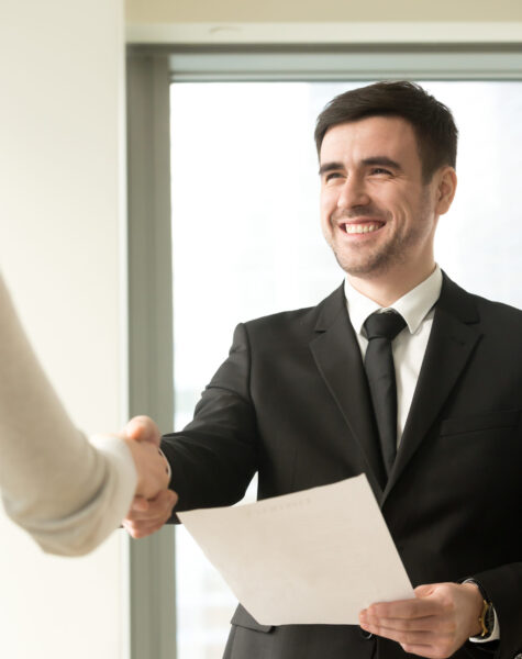 Happy smiling businessman wearing suit shaking female hand, holding document, company director congratulating new hire employee offering employment contract, awarding with diploma, vertical view